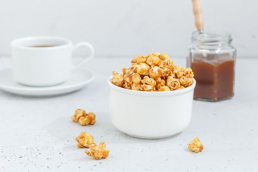 Sweet caramel popcorn in a ceramic bowl on a gray background with a jar of caramel and tea. Dessert for breakfast.