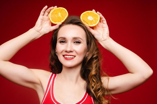 Beautiful woman in a red swimsuit with bright makeup and red lips with orange slices, summer, brightness, joy.
