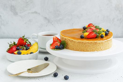 Mango cheesecake decorated with berries, mango slices and flowers on a stand.