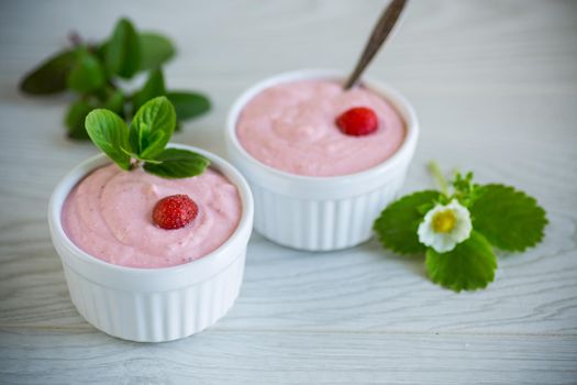 sweet curd mass whipped with fresh strawberries in a bowl, on a wooden table.