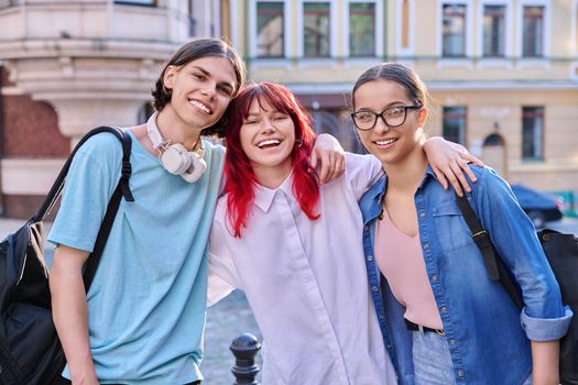 Happy smiling teenage friends hugging, looking at camera outdoor, on city street. Friendship, community, youth, lifestyle, leisure, fun concept