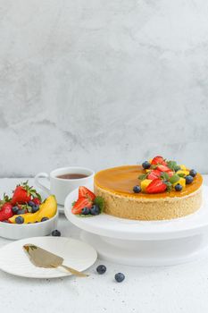 Mango cheesecake decorated with berries, mango slices and flowers on a stand. Vertical photo