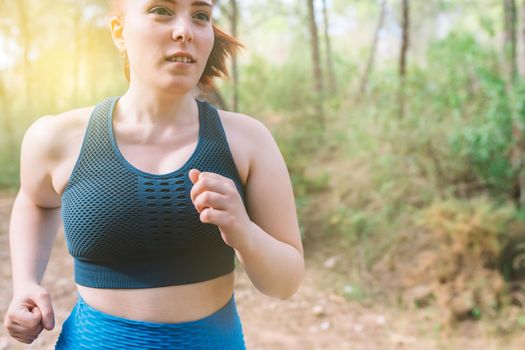 pretty young red-haired woman, running on a forest trail in the open air on a summer day.female athlete doing sport outdoors. concept of wellness and healthy life. outdoors, natural sunlight.