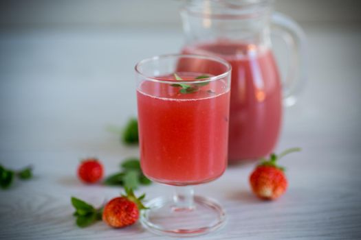 Cold summer strawberry kvass with mint in a glass on a wooden light table