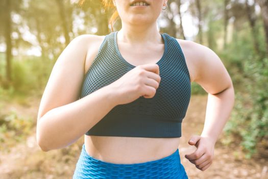 cropped shot young woman running through a forest on a summer day. female athlete doing sport outdoors. wellness and healthy living concept. outdoors, natural sunlight.