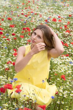 a beautiful young blonde woman in a yellow dress stands among a flowering field of poppies, daisies, cornflowers and laughs. High quality photo