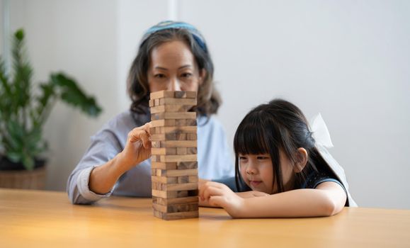 Happy moments of Asian grandmother with her granddaughter playing jenga constructor. Leisure activities for children at home