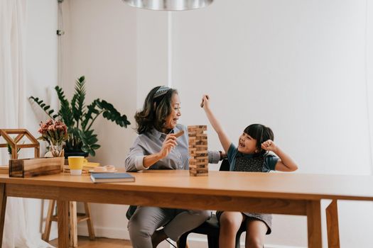 Happy exciting moments of Asian grandmother with her granddaughter playing jenga constructor. Leisure activities for children at home