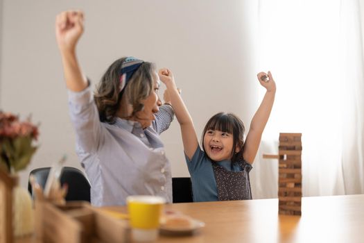 Happy moments of Asian grandmother with her granddaughter playing jenga constructor. Leisure activities for children at home