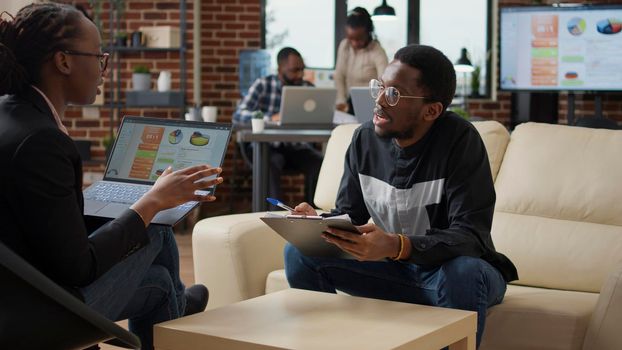 Woman explaining data charts on laptop and man taking notes on documents, doing job collaboration to create financial analysis strategy. Business people working together to plan project.