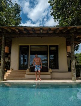 European man at infinity pool in Thailand looking out over the ocean, luxury vacation in Thailand, private pool villa. High quality photo