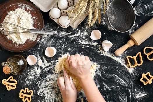 Woman's hands knead dough on table with flour, eggs and ingredients on black table. Top view. Still life. Flat lay