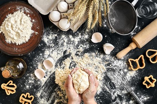 Woman's hands knead dough on table with flour, eggs and ingredients on black table. Top view. Still life. Flat lay