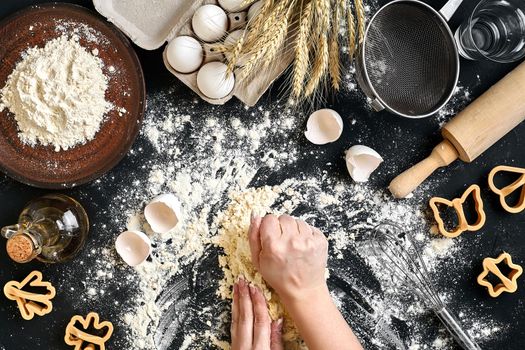 Woman's hands knead dough on table with flour, eggs and ingredients on black table. Top view. Still life. Flat lay