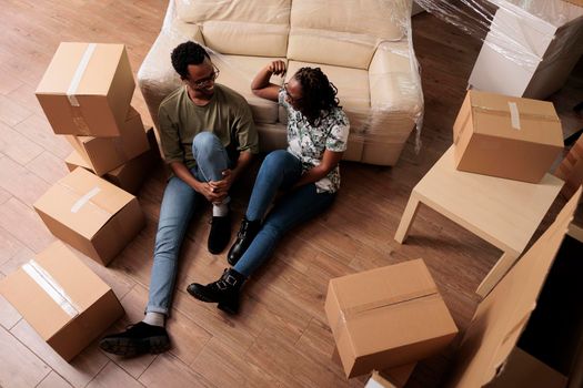 African american couple enjoying new household property, taking break on floor after moving in together. Relaxing on moving day, buying first apartment home on mortgage loan. Top view of.