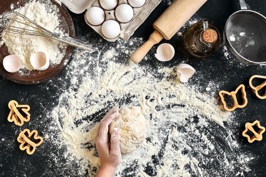 Woman's hands knead dough on table with flour, eggs and ingredients on black table. Top view. Still life. Flat lay