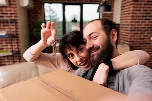 Happy man and woman holding keys of property bought on loan, buying first house together as family. Celebrating lifestyle achievement and moving in new apartment flat to start family.