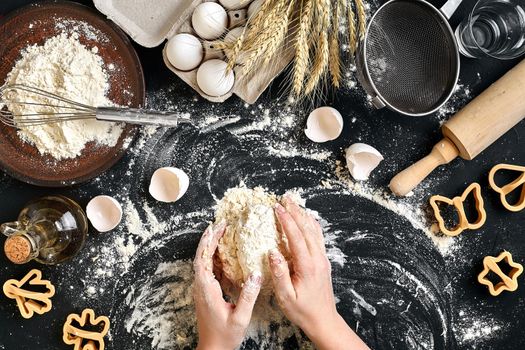 Woman's hands knead dough on table with flour, eggs and ingredients on black table. Top view. Still life. Flat lay