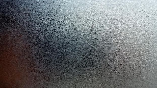 Abstract frosty pattern on glass, background texture. Frozen windshield. Granular structure of transparent ice. The sky is shining through. Abstract ice background.