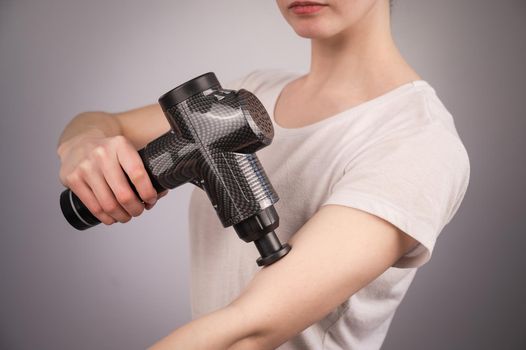 Caucasian woman uses a massager gun for pain in the muscles of the arm