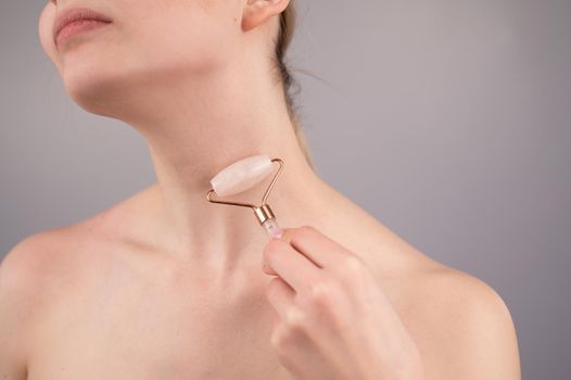 Close-up portrait of a woman using a quartz roller massager for an alternative fight against wrinkles on her neck. Smoothing of the rings of venus