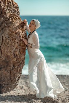 Middle aged woman looks good with blond hair, boho style in white long dress on the beach decorations on her neck and arms