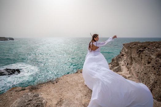 Happy freedom woman on the beach enjoying and posing in white dress. Rear view of a girl in a fluttering white dress in the wind. Holidays, holidays at sea