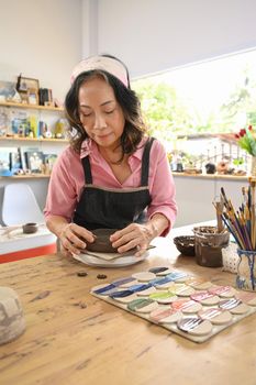Retired woman creating handicraft crockery in art workshop. Retirement, activity, Art ceramic and hobby concept.