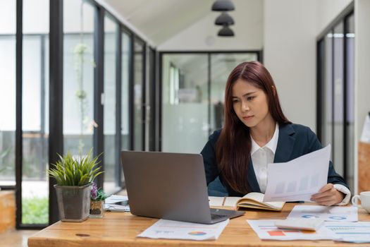 Concentrated young asian businesswoman working with paperwork and laptop computer. accounting finance concept