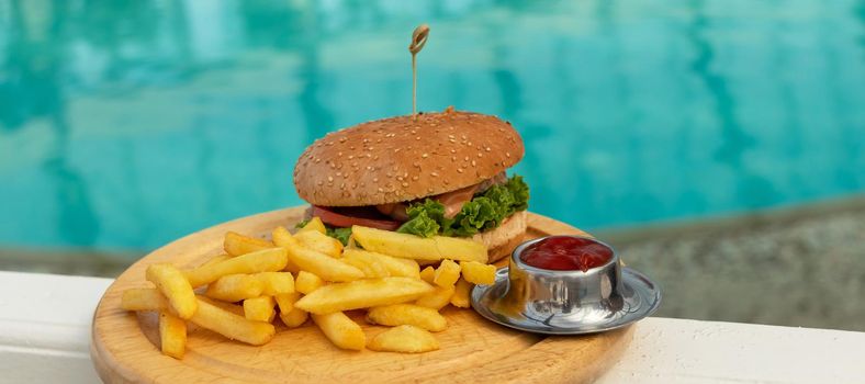 banner with tasty hamburger, appetizing french fries and ketchup. concept of relaxing and eating by the sea on a bright, hot and sunny day on the beach. soft focus. copy space