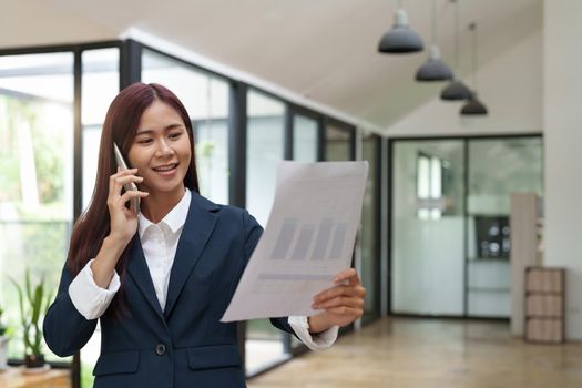 Young asian business woman talk on cellphone discussing paperwork