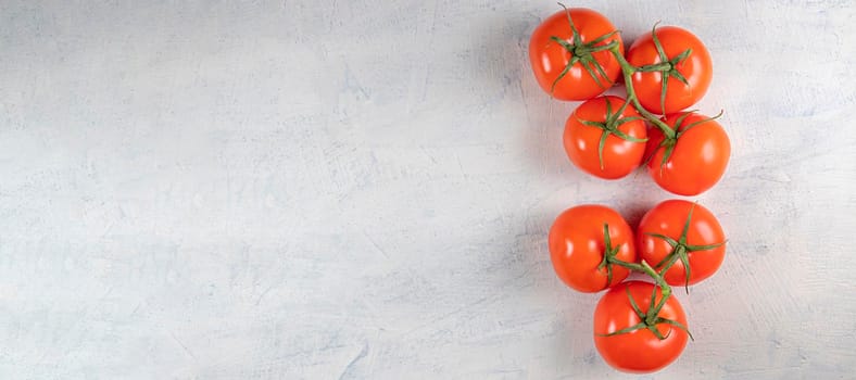 banner with seven red fresh and tasty tomatoes on a green twig on a white stone background. Top view. Copy space