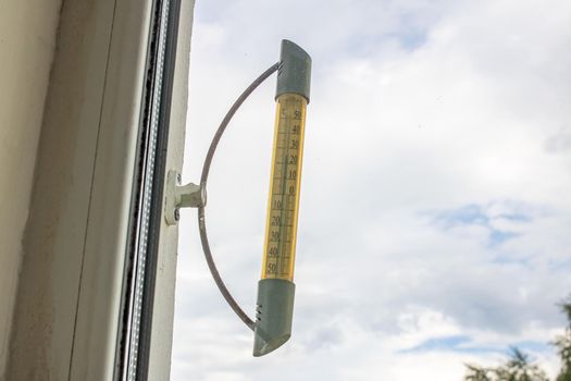 Outdoor thermometer on the window close up on sky background
