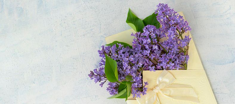 banner with Very Peri color lilac flowers in festive envelope with bow on textured background. the concept of summer, spring, nature bloom, holiday and congratulations. copy space. flat lay. top view