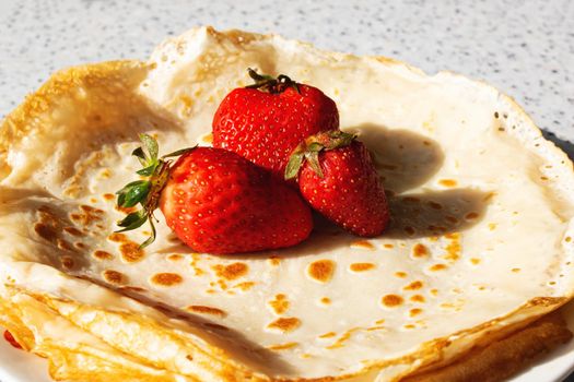 Yellow pancakes and strawberries on a plate close up