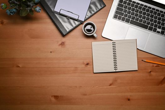 Simple workspace with laptop computer, notebook and clipboard on wooden table.