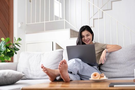 asian young woman looking laptop laughing with good news or discount voucher for shopping online at home.Happy and cheerful woman looking on laptop read message feel excited.