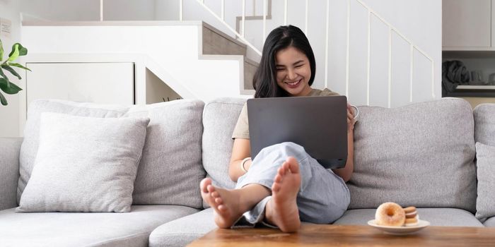 asian young woman looking laptop laughing with good news or discount voucher for shopping online at home.Happy and cheerful woman looking on laptop read message feel excited.