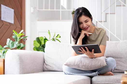 Attractive smiling young asian woman relaxing on a leather couch at home, working on laptop..