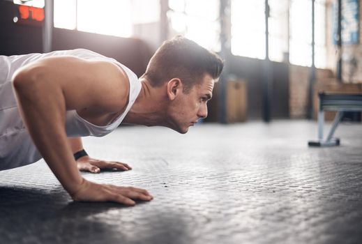 Shot of a young man doing pushups in a gym.