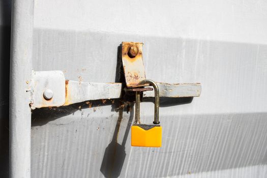 Yellow padlock on a gray metal door close up