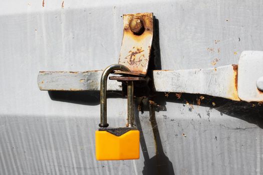 Yellow padlock on a gray metal door close up