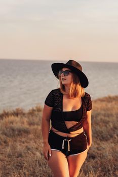 Vertical Portrait of Young Woman in Hat and Sunglasses Posing on the Background of Sea at Sunset