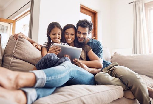 Shot of a mother and father using a digital tablet with their daughter on the sofa at home.