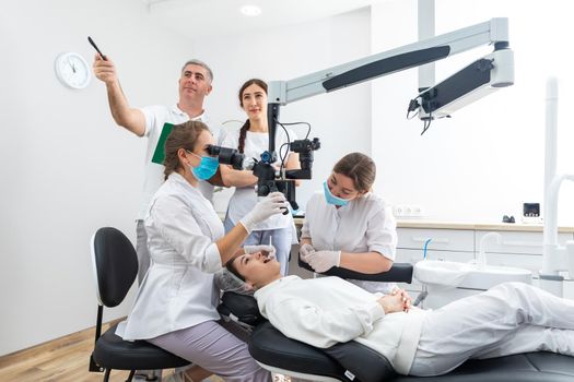 Group of students in dental clinic learn watching dental treatment with microscope