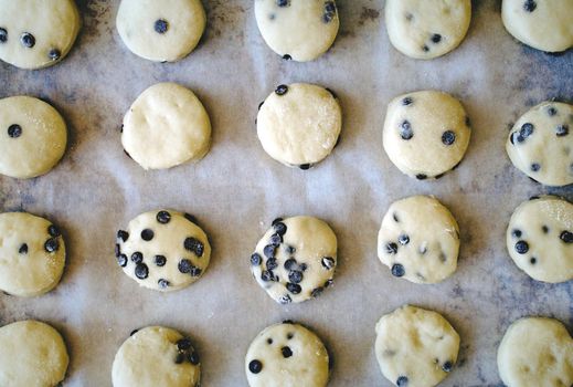 Chocolate chip cookies (or biscuits) on baking paper on a tray ready to go in the oven