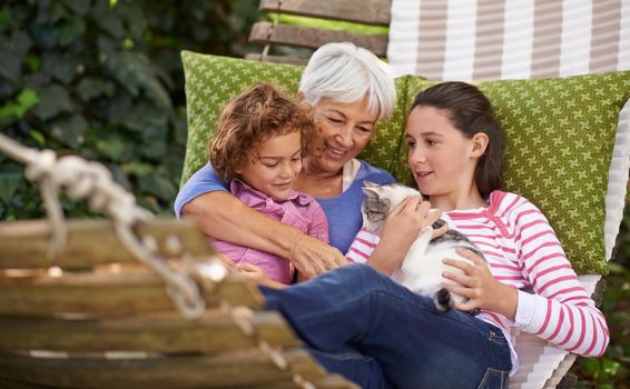 Shot of a grandmother and her grandchildren sitting outside on a hammock together with a cat.