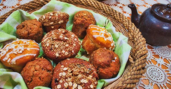 Basket full of freshly baked muffins on a table with a teapot