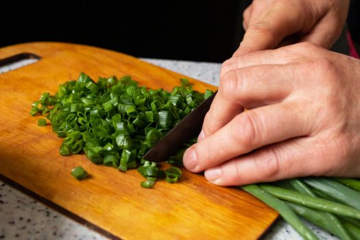 Hands cut green onion on a wooden board close up