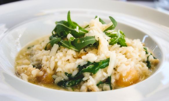Pumpkin risotto with rocket leaves and parmesan cheese shavings in a white dish